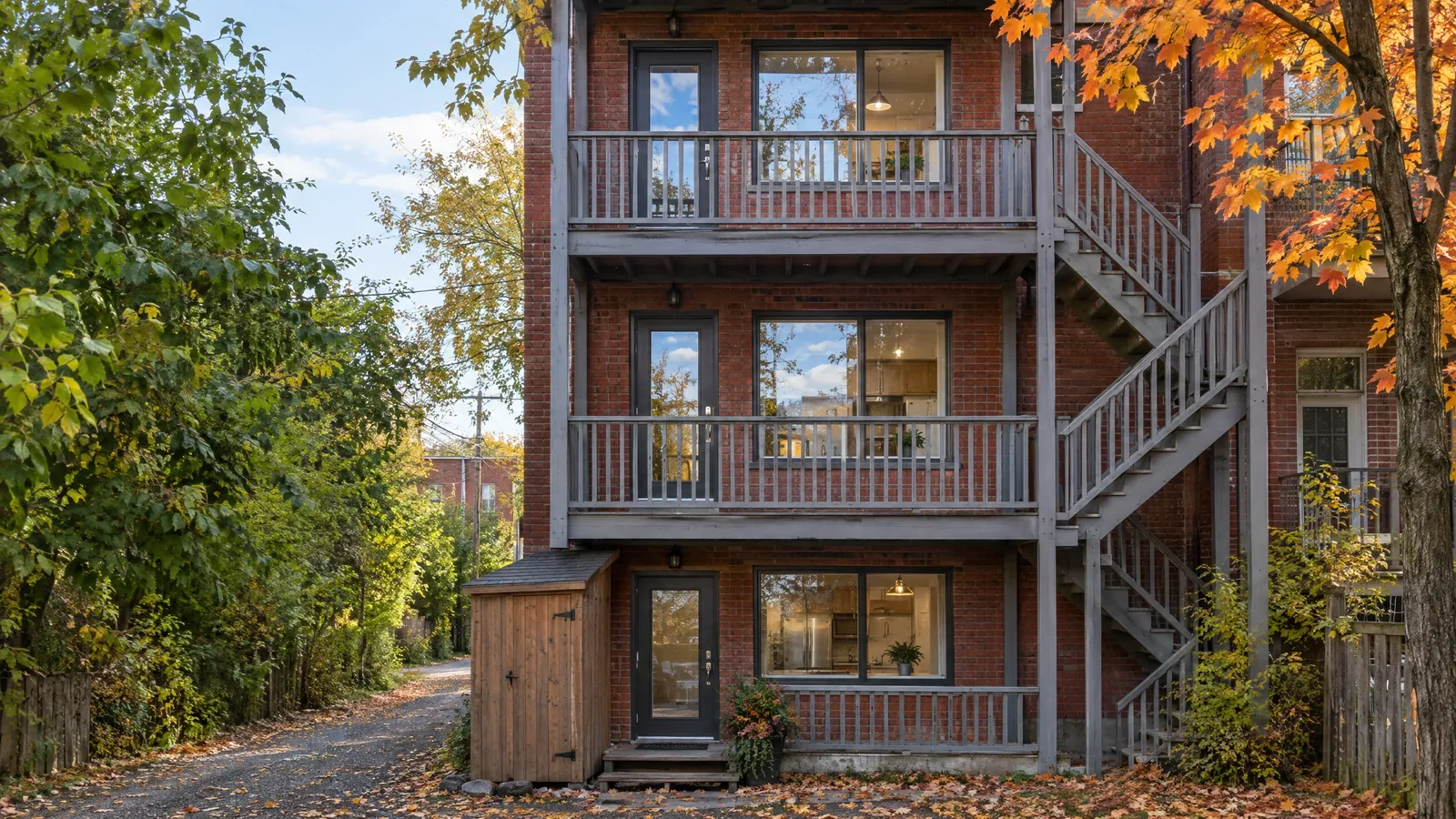 Back of a red-brick triplex in autumn, a glass door on each floor opening onto wooden galleries and an outside staircase