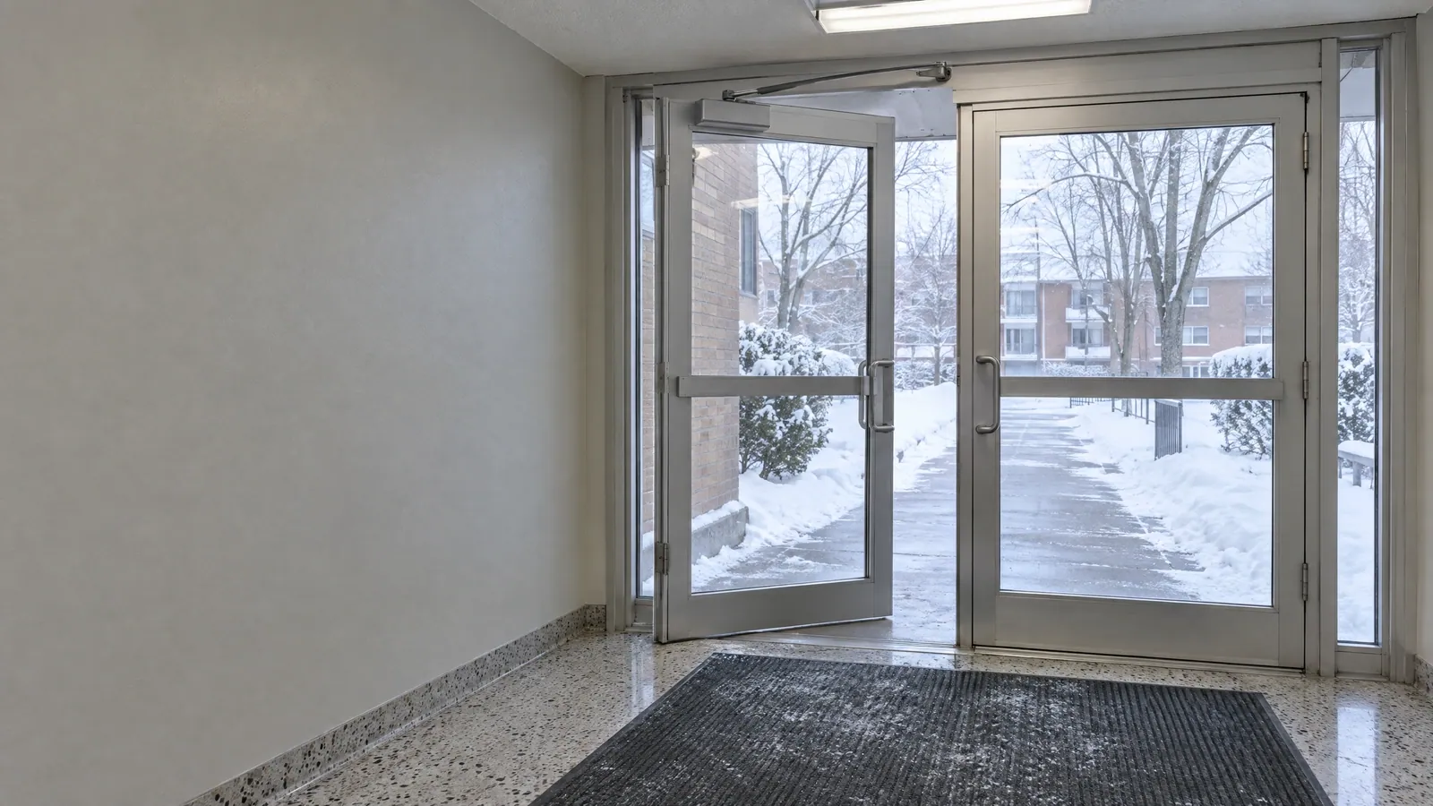 Aluminum-framed glass entrance door with an overhead door closer, seen from inside a cold building vestibule